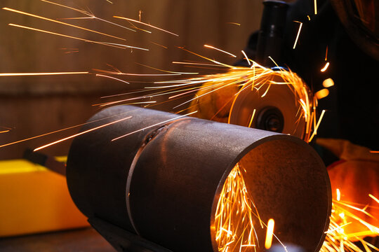 Angle grinder cutting a metal pipe with flying sparks.