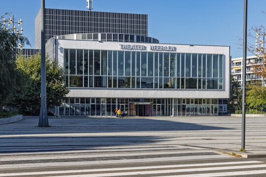 Heerlen, Netherlands - 04 October 2026: Exterior view of Theater Heerlen featuring its prominent modern glass facade and large open paved plaza on a sunny autumn day.