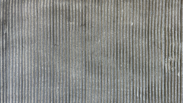 Close-up of a finely grooved gray surface with evenly spaced vertical lines, creating a minimalist geometric texture and subtle abstract background with strong visual rhythm.