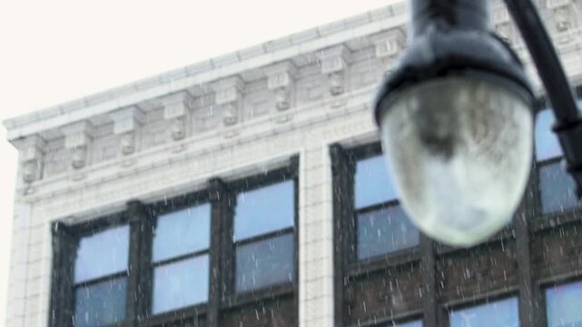 Close up of street lamp while snow is coming down in the city