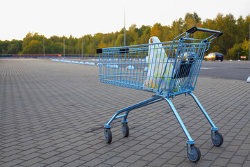 Metal shopping cart with a plastic bag inside stands on a paved parking lot outside a supermarket © yaviki