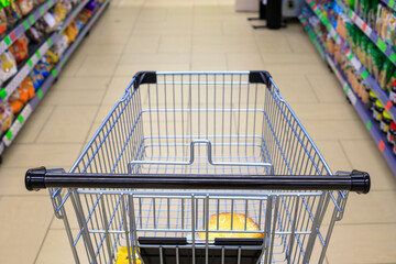 First-person view of a metallic shopping cart moving through a supermarket aisle between shelves stocked with products © yaviki