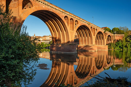 An morning view of the historic old town of Albi as the sun sets, featuring the Pont Neuf (New Bridge, also known as the Bridge of August 22, 1944), which spans the river Tarn.