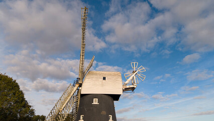  windmill low angle view: Traditional old wind mill tower with large wooden sails and cloudy blue sky background, historical landmark and heritage architecture photography. © Serhii