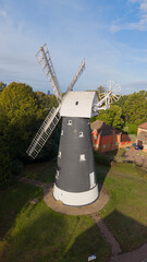  windmill aerial view: Traditional old wind mill tower with wooden sails in British residential suburb, heritage architecture, green lawn landscape, and sunny day photo. © Serhii
