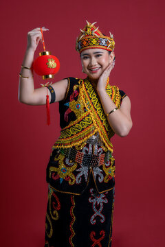 Young women in Kenyah Orang Ulu traditional clothing holding a red Chinese lantern on red background Chinese New Year Concept