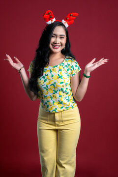Portrait of young woman in yellow theme cloth with Christmas headband on red background