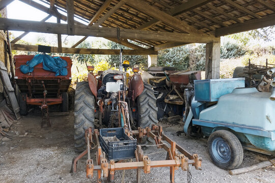 Vintage red tractor parked in an old rustic barn with traditional agricultural machinery and farm equipment