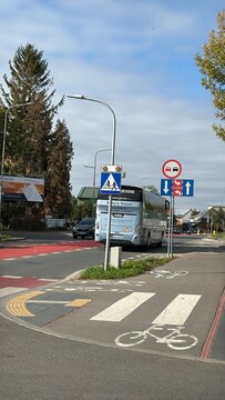 Zamosc, Poland on October 10, 2026. A large silver tour bus drives through a city intersection with a red lane marking and green trees under a cloudy sky, commercial transit, tourism concept.