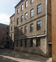 A multi-story brick residential building overlooking a quiet inner courtyard, with weathered masonry, rows of windows and sunlight casting long shadows across the pavement. An example of traditional u © Martin