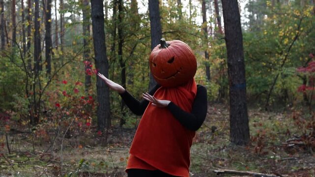 Girl with a pumpkin instead of a head dances merrily on a forest path, celebrating Halloween. Halloween celebration. Character with a carved Jack-o-lantern on her head dances in a pine forest.