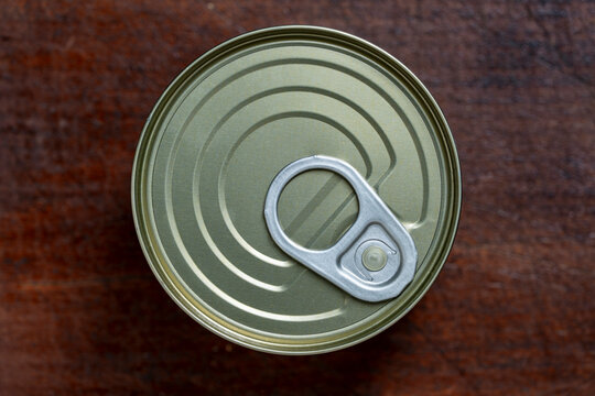 Tin can with easy open ring pull top view on wooden table. Top view of closed green metal tin can. Aluminum canned food package with pull tab ring for grocery, storage and survival concepts