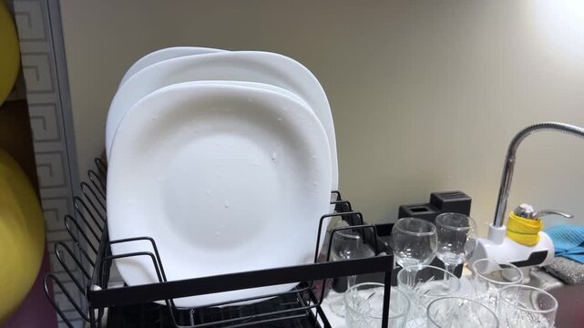 Woman placing clean plates into a dish drying rack after washing dishes showing kitchen organization and everyday household cleaning routine. High quality FullHD footage