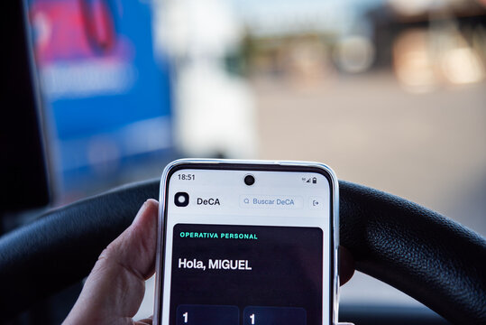 Truck driver holding a smartphone displaying the DeCA electronic transport document app inside a truck cab