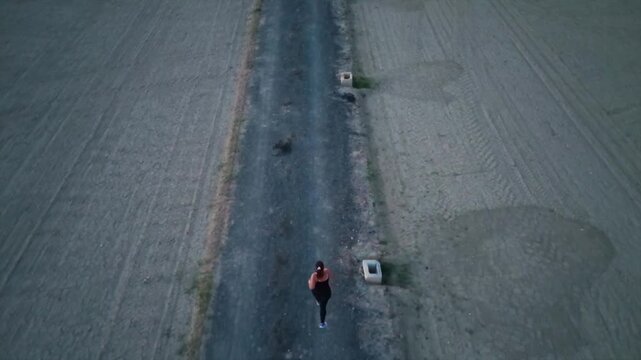 Aerial top-down shot of a young woman running on a dirt path in the countryside at dusk
