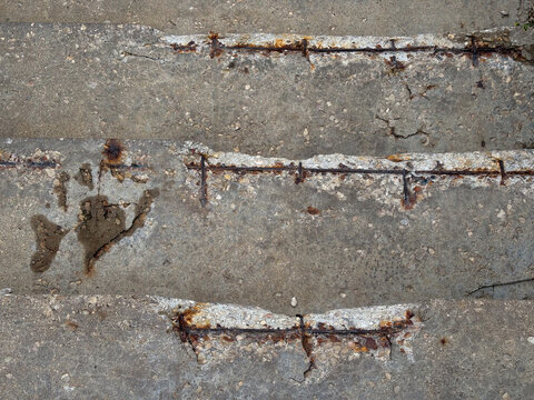 Close-up texture of cracked and deteriorating concrete with reddish-brown rust stains from corroding steel reinforcement. Rough surface, structural damage and material degradation