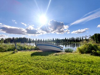 Small rowing boat tied on green grass bank at peaceful lake on bright summer day. © Rin