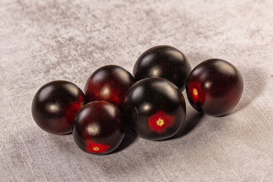 Gray textured surface with six dark cherry tomatoes showing deep red undertones and golden calyxes, fresh produce closeup