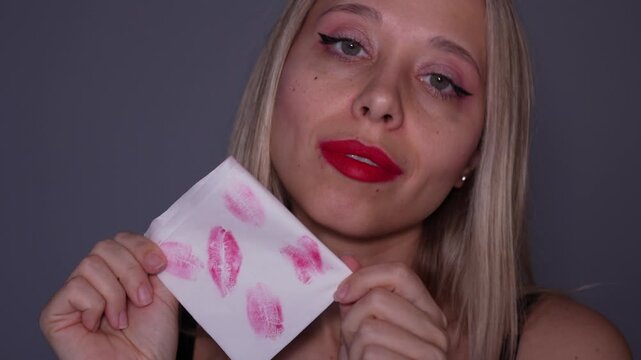 Young woman showing a tissue with red lipstick kiss marks, testing makeup transfer after applying bold lipstick