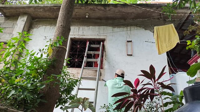 Young Worker Removing Old Wooden Piece from Wall near Window