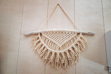 Beige macrame wall hanging decoration on a wooden stick against a neutral wall, handmade fiber art, boho home decor. © Hanna
