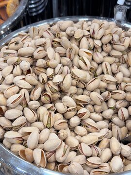 Open shell roasted pistachios fill a reflective metal tray, showing beige shells, green kernels, and varied natural shapes in close detail
