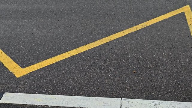 A yellow arrow painted on the road next to a curb, often used as a guide or direction