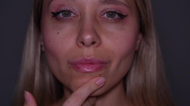 Young blonde woman gently strokes her cheek, showing a refined face contour and smooth skin after buccal fat removal in a soft beauty portrait