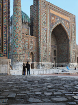 Registan Square with a couple admiring the Sher-Dor Madrasah fa&ccedil;ade in Samarkand. Monumental Islamic architecture with turquoise tilework ideal for travel and tourism visuals.