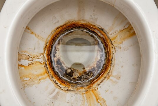 Dirty toilet bowl with heavy rust limescale mineral buildup and stains requiring deep cleaning and plumbing maintenance