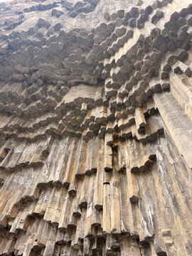 Garni, Armenia - August 26, 2026: Close view of dark hexagonal basalt columns projecting from a tall weathered rock wall with layered textures and angular formations