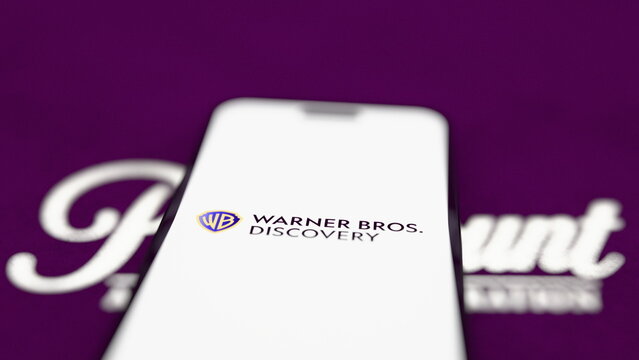 The Warner Bros. Discovery logo on a smartphone, with a projected Paramount logo. A judge approves Paramount's $110 billion takeover of Warner Bros. Discovery. October 4, 2026, Lisbon, Portugal.