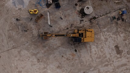 Top-down aerial view of a large excavator surrounded by construction equipment, temporary fencing, pipes and building materials on an active groundworks site in England. © ADS Media