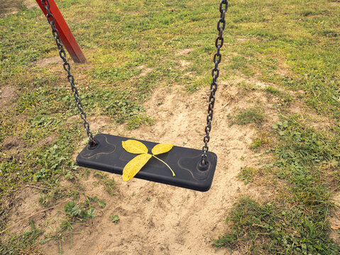 Empty Playground Swing With Yellow Fallen Leaf On Black Seat In Autumn Park