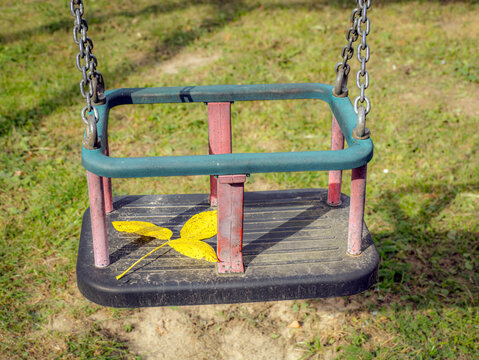 Empty Child Swing With Bright Yellow Leaf on Worn Playground Seat in Autumn Park
