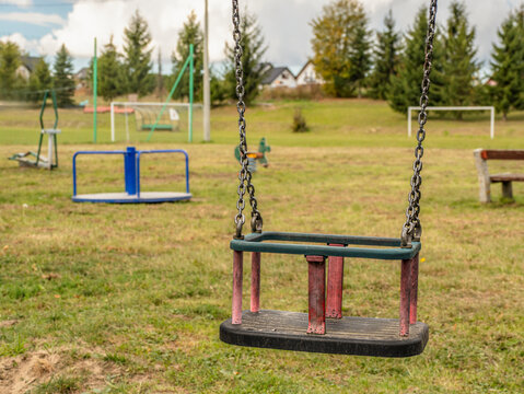 Empty Child Swing in Quiet Park Playground With Grass and Distant Equipment