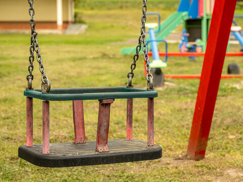 Empty Worn Toddler Swing Seat Hanging In Outdoor Playground On A Sunny Day