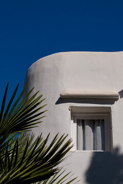 Ibiza, Balearic Islands, Spain: the curved corner of a white Mediterranean style building with a small recessed window and palm fronds in the foreground under a deep blue sky in Punta Arab&iacute;