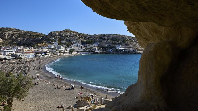 Neolithic caves, former hippie paradise, view from a cave onto a busy beach with a small town under bright blue sky, Matala, south coast, Crete, Greek Islands, Greece