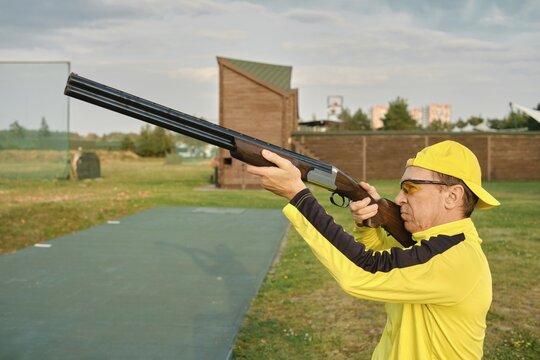 An old man shooting at an outdoor shooting range with a shotgun in hand, aiming for the target