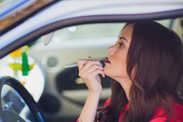 Young woman in car applying lipstick while looking into mirror, focused grooming moment, natural daylight interior scene, casual commute preparation, closeup profile portrait © Евгений Вершинин