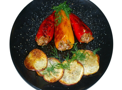 Homemade grilled sweet peppers stuffed with ground beef with crisp potato slices on a black plate