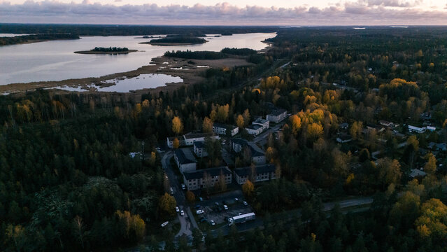 Aerial view of a residential area nestled within a dense forest and autumn foliage near a calm lake in Southern Finland, Finland.