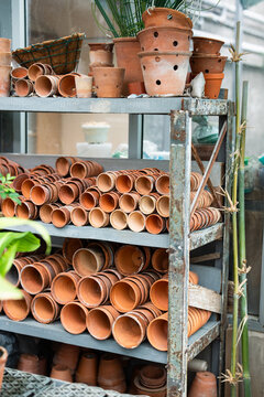 Orangery supply and tools, terracotta flowerpots stacked on shelves of rack in greenhouse warehouse, empty ceramic pots organized on metal shelves in plant nursery room, horticulture and gardening.