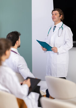 Male medical speaker gives lecture, uses paper document presentation materials shorthand dictation. Professional meeting, medical council