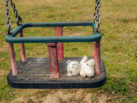 Abandoned Teddy Bear Lying on Empty Toddler Swing in Sunny Playground