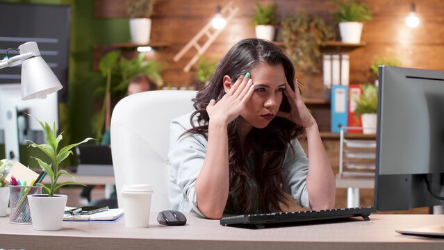 Stress, businesswoman and headache as a tired professional presses both temples at her computer, for workplace pressure, fatigue, burnout, overwork, job strain and employee wellbeing in an office.