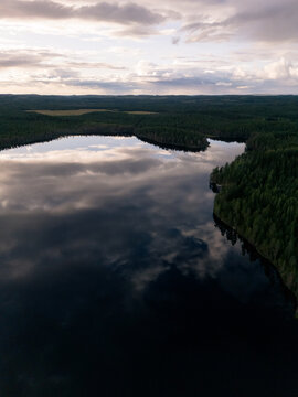 Aerial view of Eastern Finland featuring a serene lake surrounded by dense coniferous forests reflecting the dramatic cloudy sky at sunset, Finland.