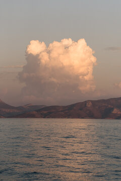 Aerial view of a large cumulus cloud glowing in the warm light above the Aegean Sea near the coastline of Kos, Greece.