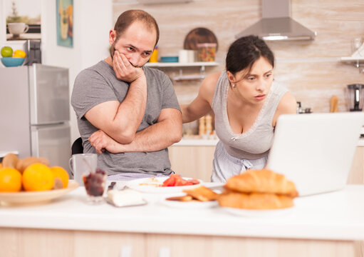 Concern, computer and couple examining a laptop screen at breakfast, with the woman leaning toward the display and the man looking worried for research, problem solving and shared decisions.